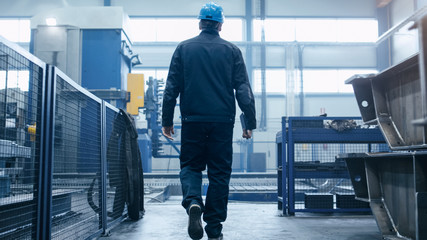 Factory worker in a hard hat is walking through industrial facilities.