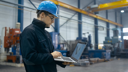 Factory worker in a hard hat is using a laptop computer with an engineering software.