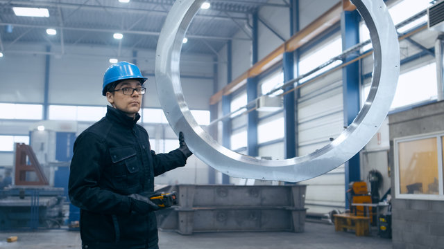 Factory Worker In A Hard Hat Is Moving A Metal Detail With A Remote Crane.