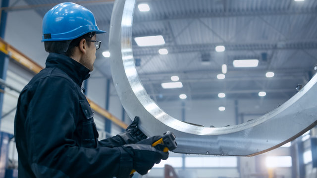 Factory Worker In A Hard Hat Is Moving A Metal Detail With A Remote Crane.