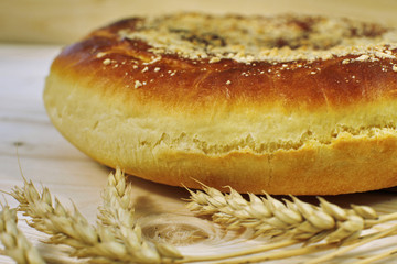 Ruddy baked onion and eggs pie with ripe wheat ears on wooden table close up