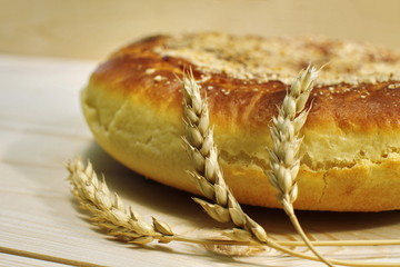 Ruddy baked onion and eggs pie with ripe wheat ears on wooden table close up