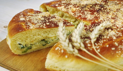 Ruddy baked onion and eggs pie with ripe wheat ears on wooden table close up