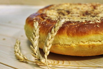 Ruddy baked onion and eggs pie with ripe wheat ears on wooden table close up