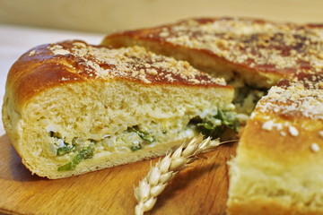 Ruddy baked onion and eggs pie with ripe wheat ears on wooden table close up