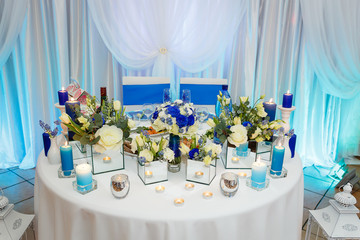 Flower and candles table decorations for wedding party in blue color - groom and bride table.