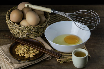 Egg in the white bowl and whisk together with peanut, chopstick and green tea on the wooden background