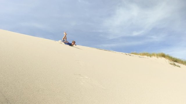 Child surfing down sand dune