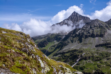 Begrünter Fels vor einem Wolkenverhangenen Bergipfel