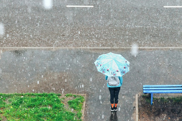 girl with umbrella standing under the rain at the bus stop