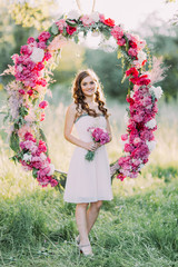 The smiling bridesmaid with the bouquet at the background of the wedding peonies arch.