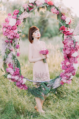 The bridesmaid with short hair in the short light pink dress and with the bouquet is standing...