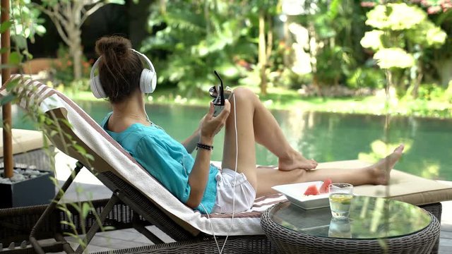 Woman listening music while relaxing on sunbed and checks handsome man out, steadycam shot
