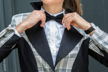 Close up of young Woman Adjusting her black bow tie in white shirt and black and gray jacket and a black bow tie