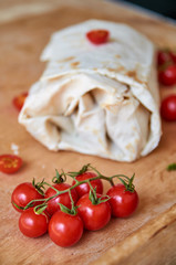 Vegetarian burrito with vegetables decorated with chopped cherry tomatoes and cardamom on blurred background. On foreground small cherry tomatoes on brown wooden background close up. Horizontal image