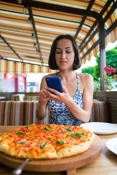 The girl is making pizza photos on the phone.