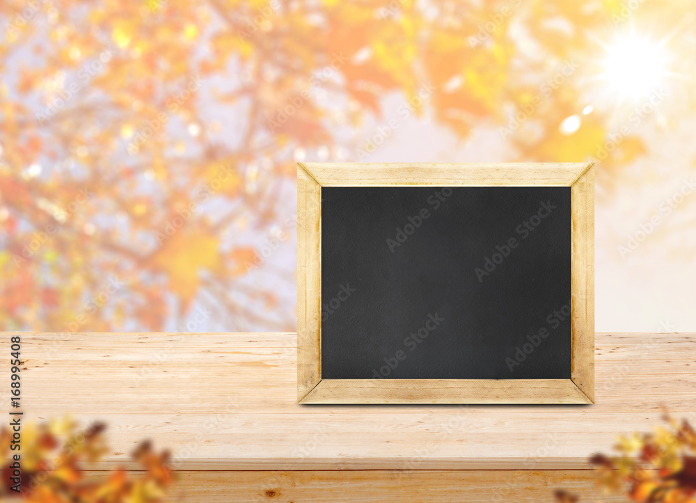 Poster blackboard on wood table top with blur maple leaf with sunlight and blurred maple leaves at foregrou