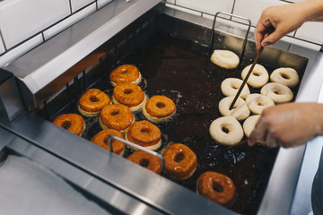 Procedure of making donuts in a small town donut bakery - putting donuts in a deep fryer. Selective...