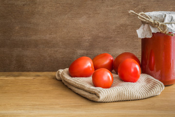 Red tomatoes with tomato paste jar on the wooden table. Rustic atmosphere. Food concept.