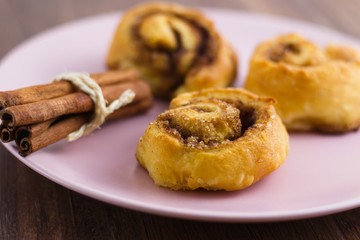 Cinnamon rolls and a pack of cinnamon sticks on pink plate ready to eat