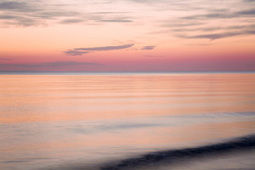 Sea water reflecting a pink heavenly colors and creating a romantic atmosphere in summer evening. Nature background.