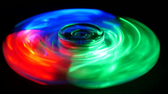 Fidget spinner with red, blue and green LED lights spinning in the dark 

