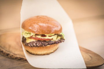 Big burger with beef and lettuce on white paper on a wooden cutting board