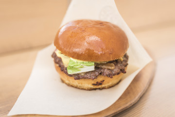 Big burger with beef and lettuce on white paper on a wooden background