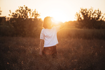 Young attractive brunette standing in the sunset summer field, contemplating