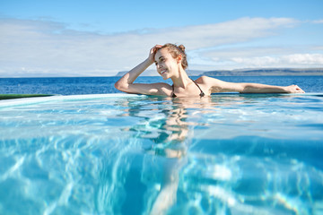 Fototapeta na wymiar Young cheerful girl swimming in water of pool looking away on background of sea, Iceland, West Fjords. back view