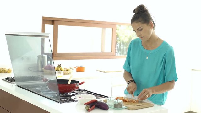 Woman looks absorbed while standing in the kitchen and cooking dinner, steadycam shot
