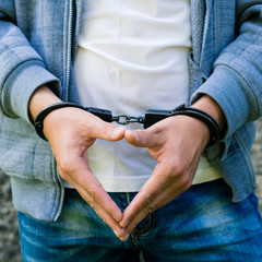 young criminal standing in handcuffs, outdoors. Concept of crime and detention