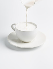 fresh milk is poured from a glass into a cup isolated on white background