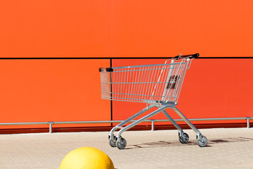 metal empty shopping cart near the orange wall of the shopping centre, copyspace for text. Concept...