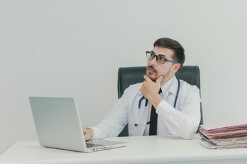 Smiling handsome male accounting office worker sitting at desk massaging his chin  while thinking  look at laptop computer screen.