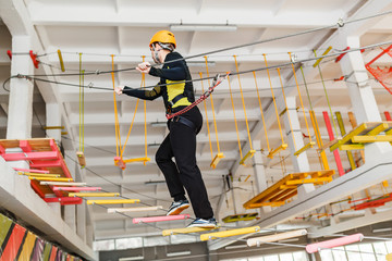 Young man climb with rope belay and helmet at indoors amusement rope park