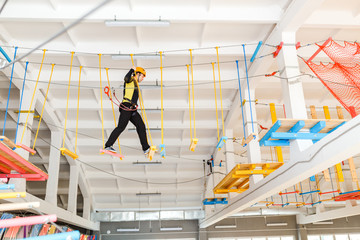 Young man climb with rope belay and helmet at indoors amusement rope park