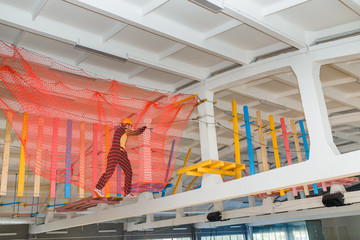 Young man climb with rope belay and helmet at indoors amusement rope park