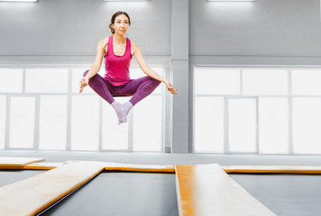 Young sports woman in yoga pose levitating in trampoline jumping fitness gym