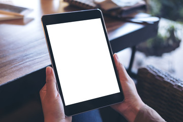 Mockup image of hands holding black tablet pc with white blank screen on wooden table background in cafe