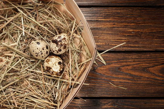 quail eggs in a straw nest over old wooden background top view