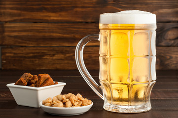 glass of cold frothy lager beer and plate of snacks on wooden table