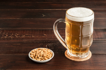 glass of cold frothy lager beer and peanuts plate on wooden table