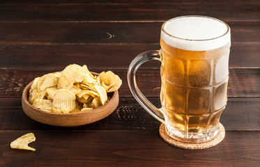 glass of cold frothy lager beer and potato chips plate on wooden table