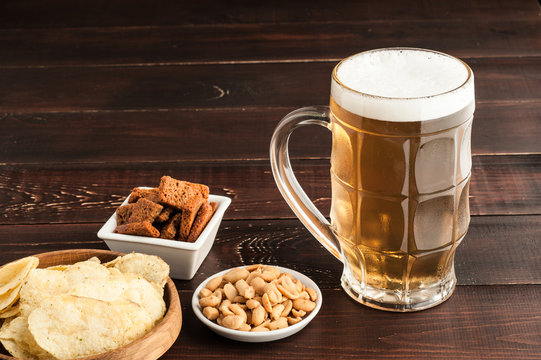 glass of cold frothy lager beer and peanuts plate on wooden table