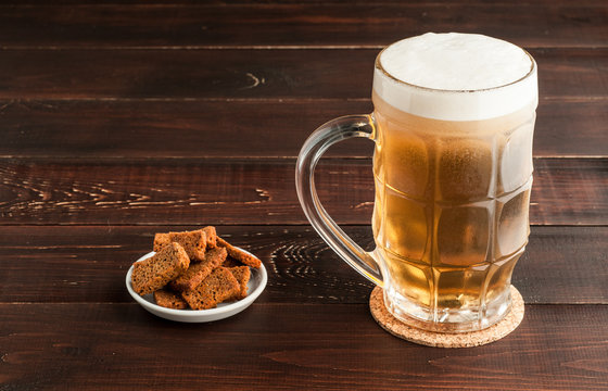 glass of cold frothy lager beer and plate of snacks on wooden table