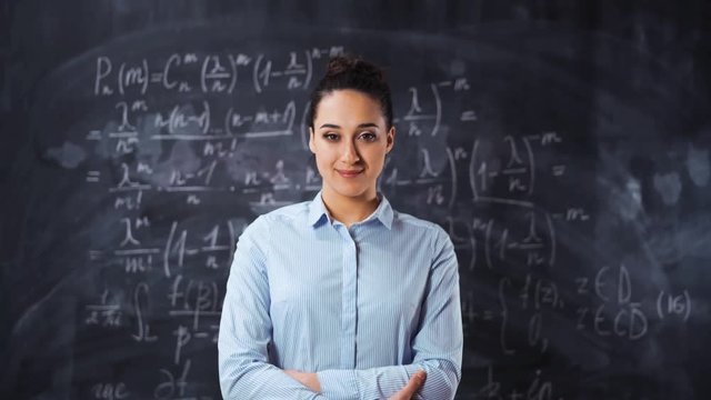 Portrait of young smart clever woman teacher lecturer standing with chalk board full of math equations at background. Lady sure in herself with crossed arms and smile a little. Glidetrack