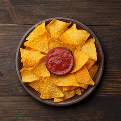 Mexican nachos or tortilla in a brown plate with dipping sauce on dark wooden background.
