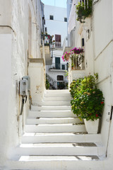 Beautiful view of scenic narrow alley with plants in romantic white city of Ostuni, Apulia, southern Italy  