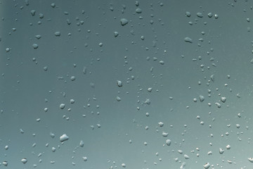 On the window a lot of different droplets from the rain. Behind the glass is visible on a background evening sky with clouds. Sunset. The window is in a small and large droplets from the rain.